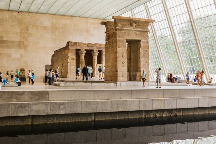 Visitors exploring the Temple of Dendur exhibit at a museum with a reflecting pool