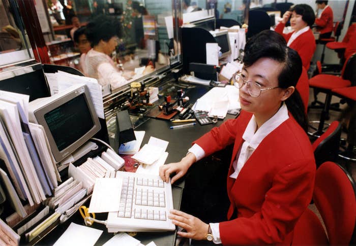 A person in a business suit working at a computer in a bustling office setting