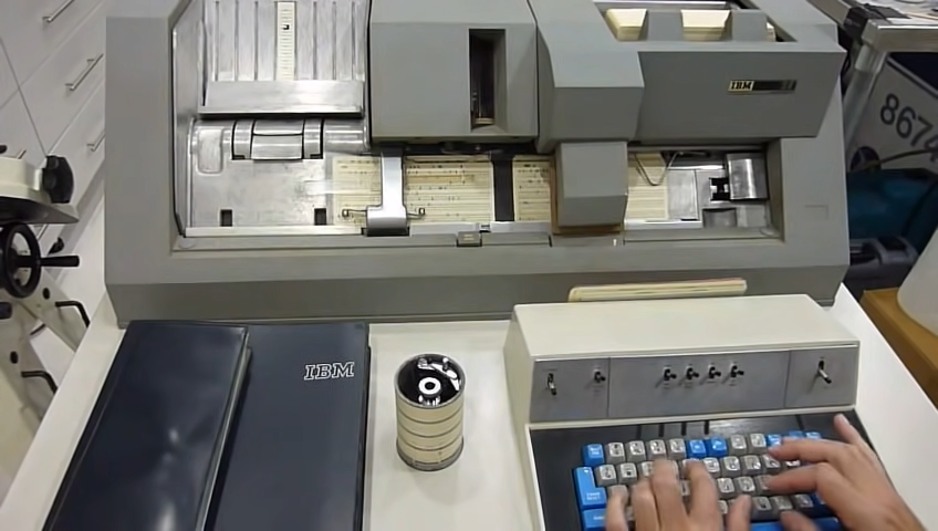 Person typing on an IBM computer punch card machine used for data entry