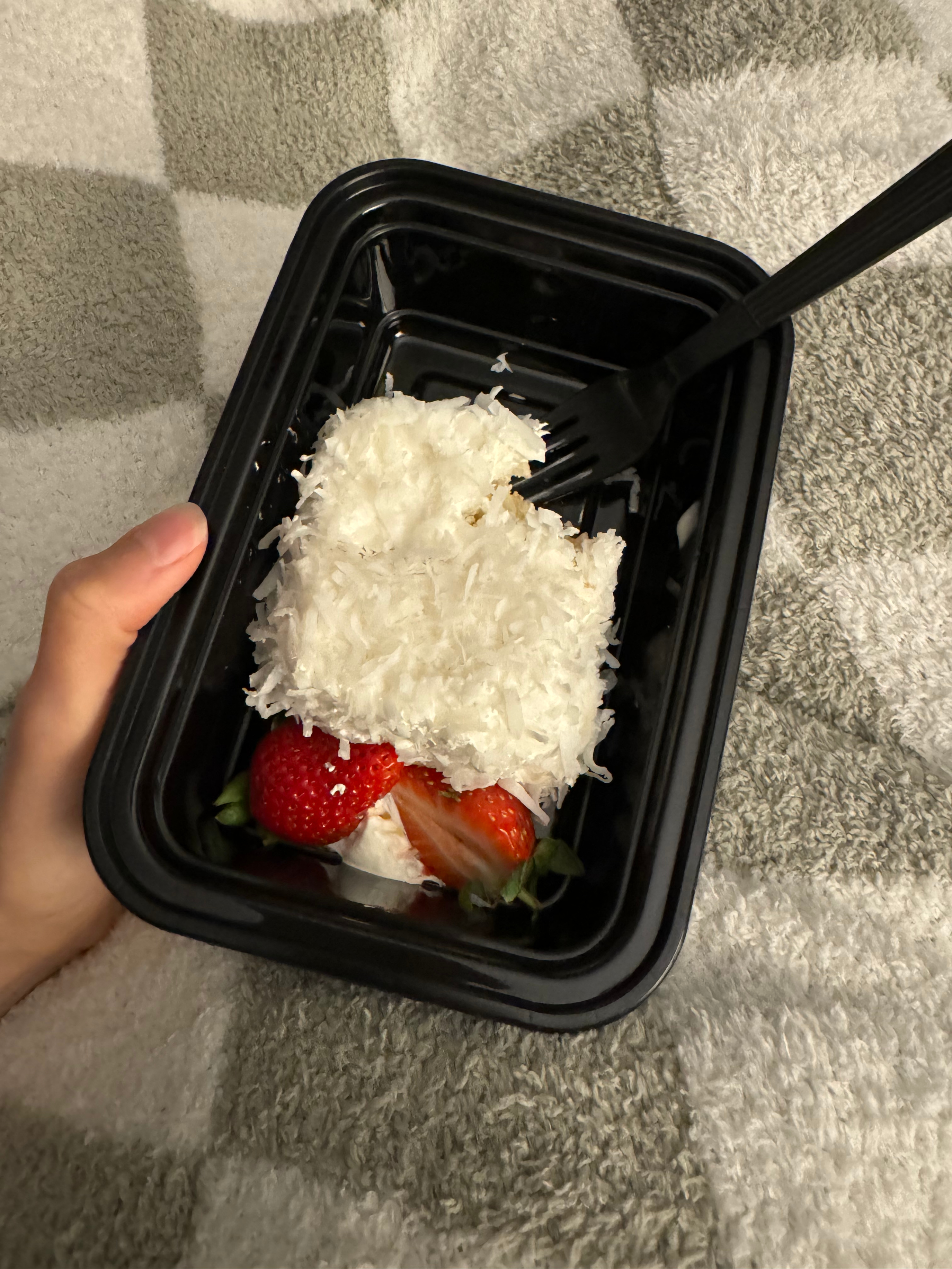 Hand holding a container with a dessert of strawberries topped with shredded coconut