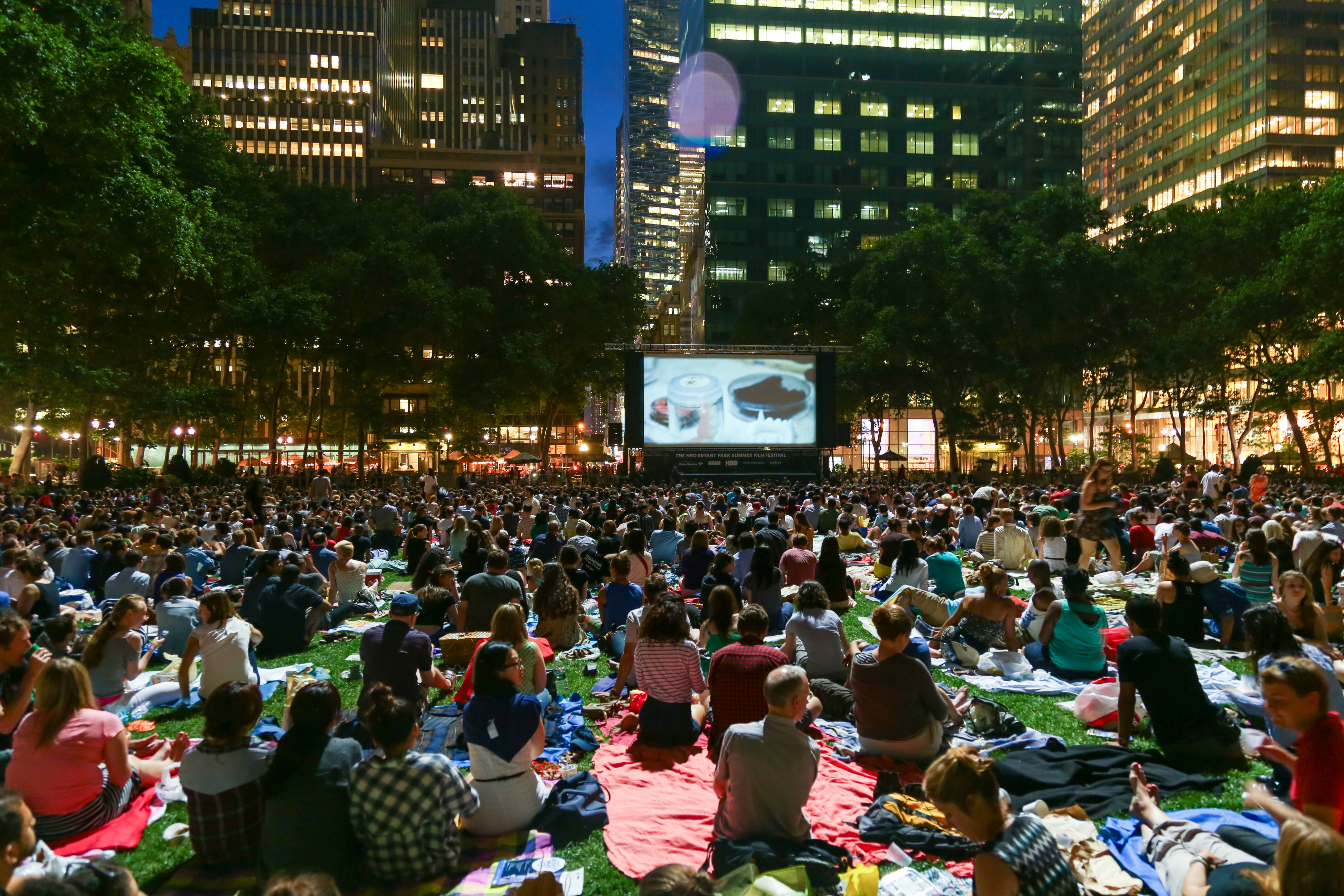 Outdoor movie screening event with large audience sitting on blankets in a park at dusk