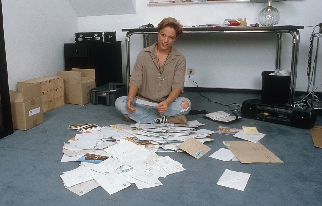 Woman sitting on floor sorting through scattered papers, indicative of financial planning or organization