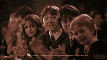 Hermione, Ron, and other Hogwarts students clapping in the Great Hall from the Harry Potter series
