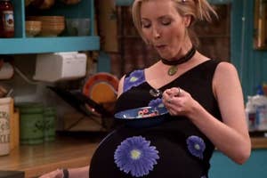 Phoebe from Friends character in a kitchen, eating from a bowl, wearing a black dress with purple flower patterns