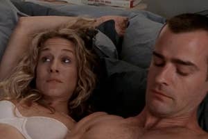 A man and a woman lying in bed side by side, with expressions of concern or disappointment