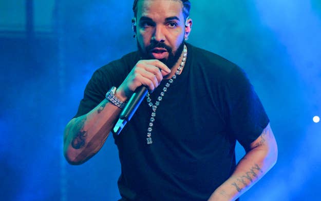 Drake performs on stage, wearing a black t-shirt and pants, with a microphone in hand