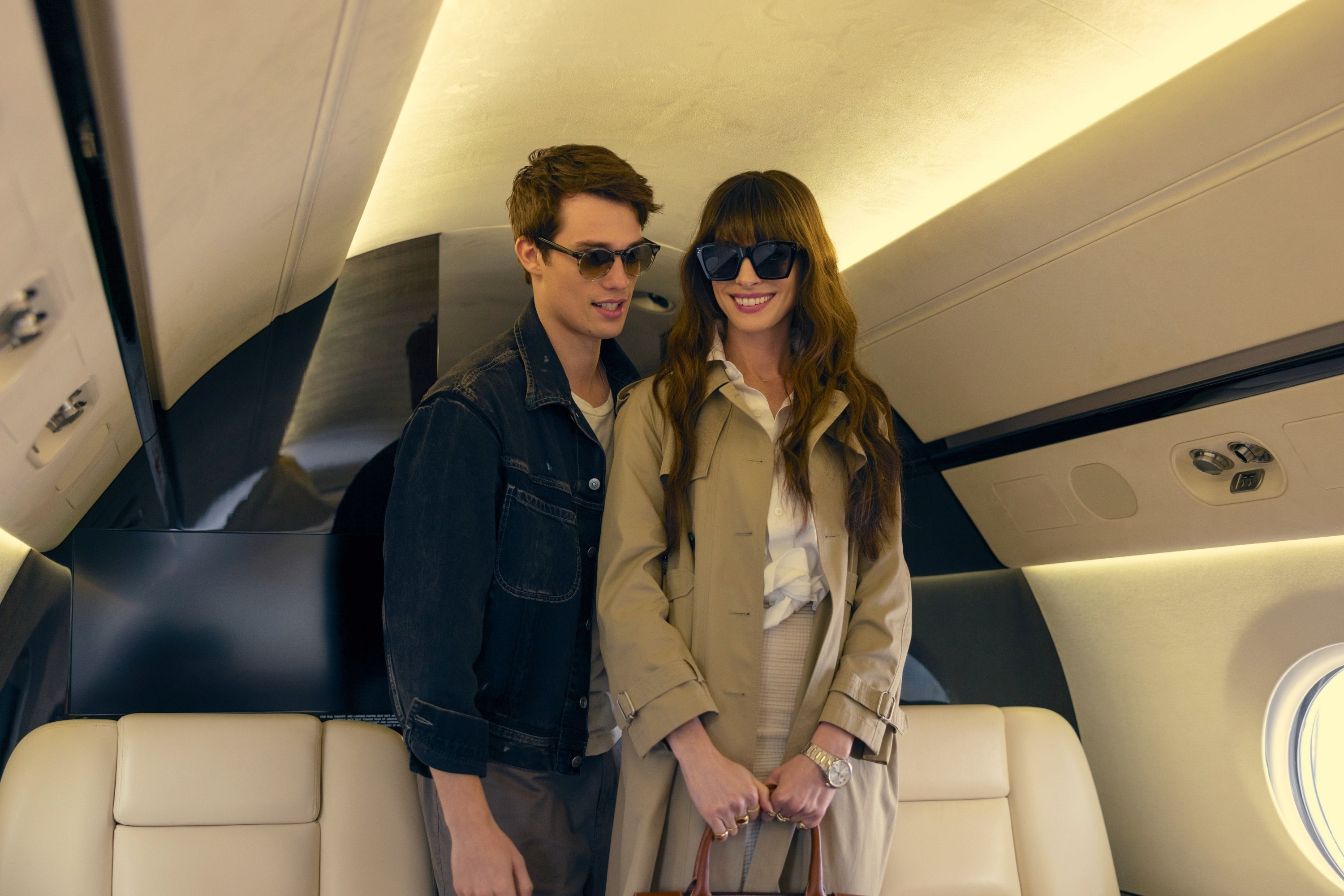 Two actors portraying characters on a TV show inside a private jet, smiling and holding hands
