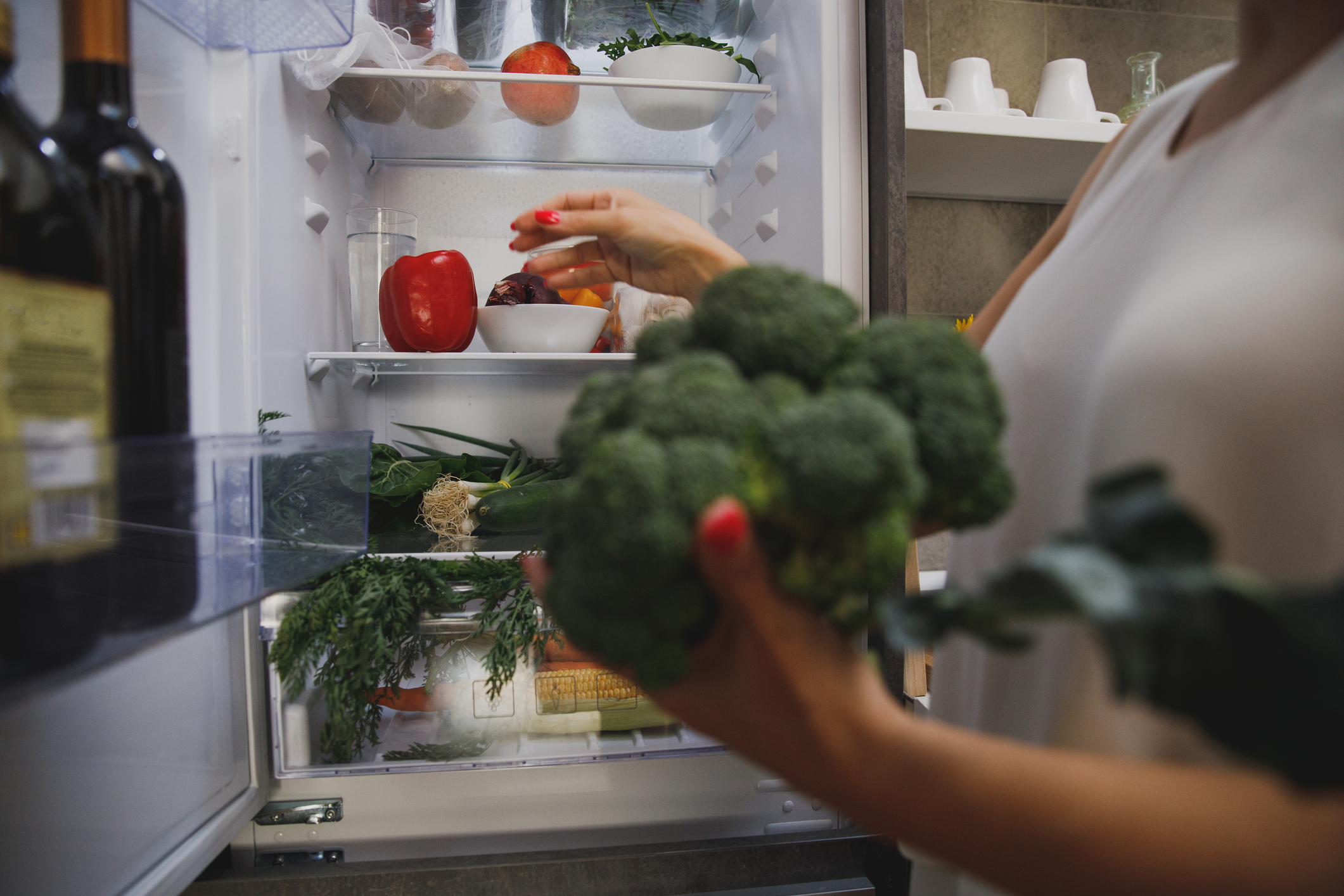 Person placing broccoli in a fridge stocked with produce and bottles
