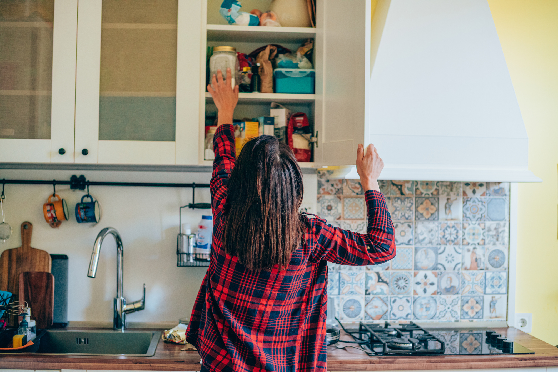Person in plaid shirt reaching for an item in a kitchen cabinet