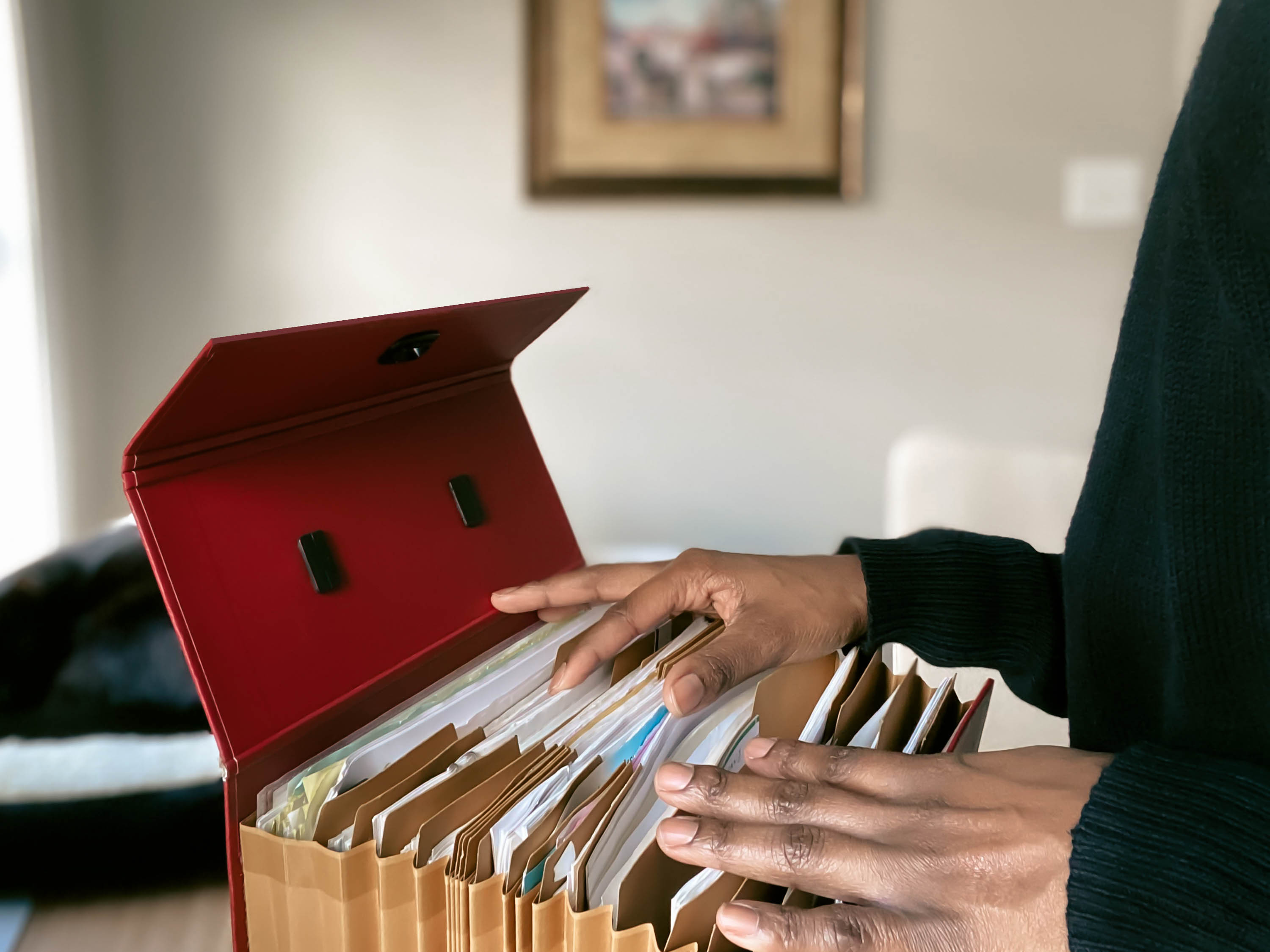 Person sorting files in a red box, standing in a room