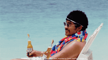Persona en playa sostiene cerveza, con gafas de sol y camisa estampada