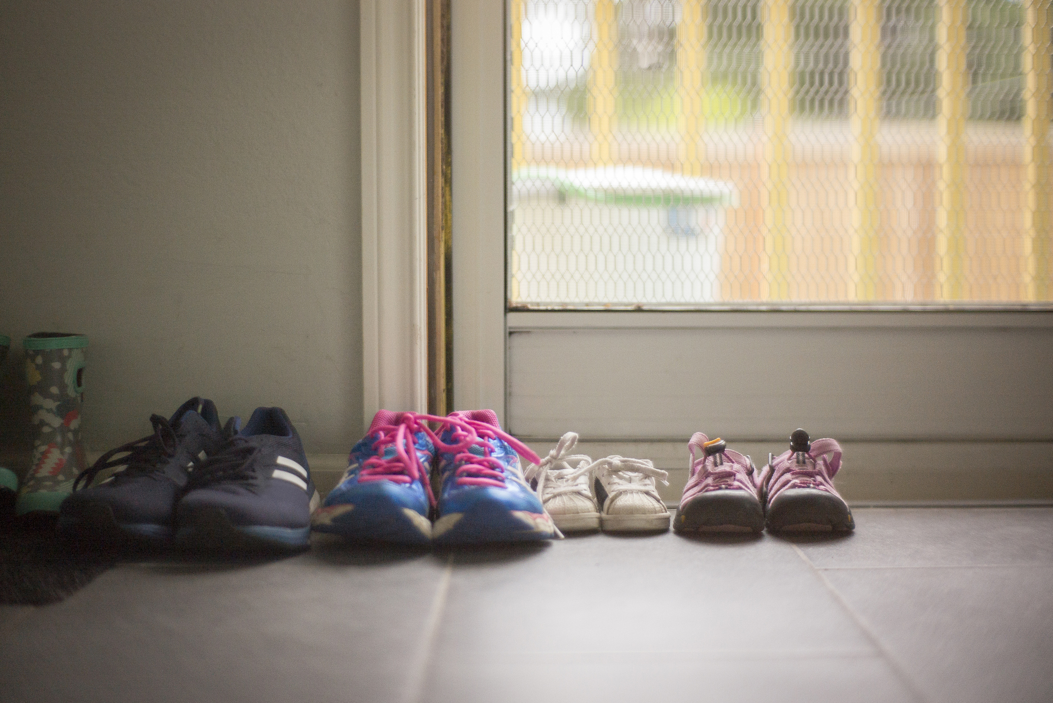 Four pairs of shoes by a door, including adult sneakers, child&#x27;s shoes, reflecting a family&#x27;s daily life