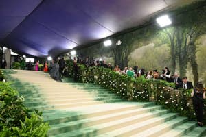 Elegant stairway lined with greenery at an event, attendees in formal wear ascending, photographers to the side
