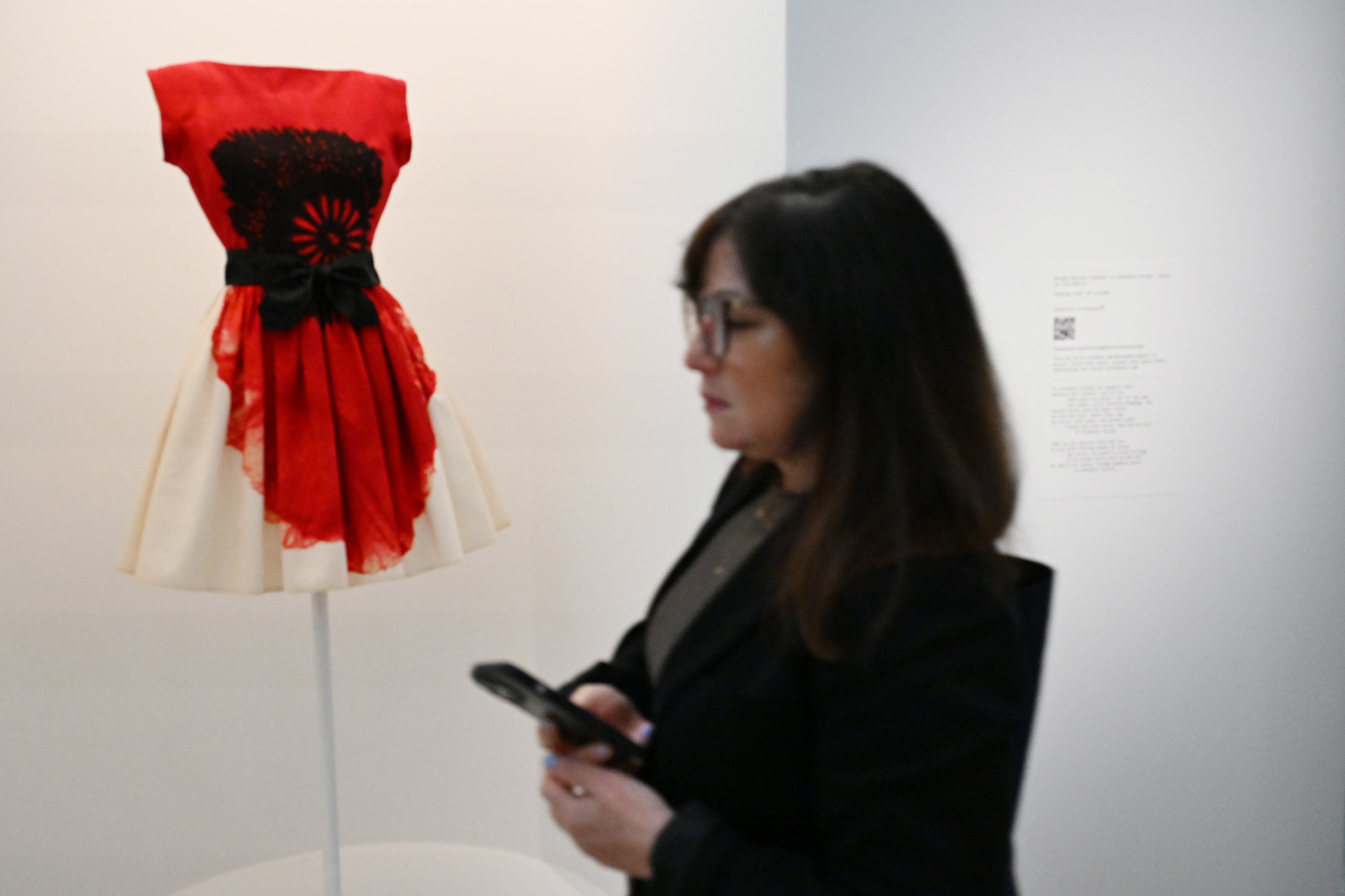 Woman viewing a red and cream dress displayed on a mannequin in a gallery