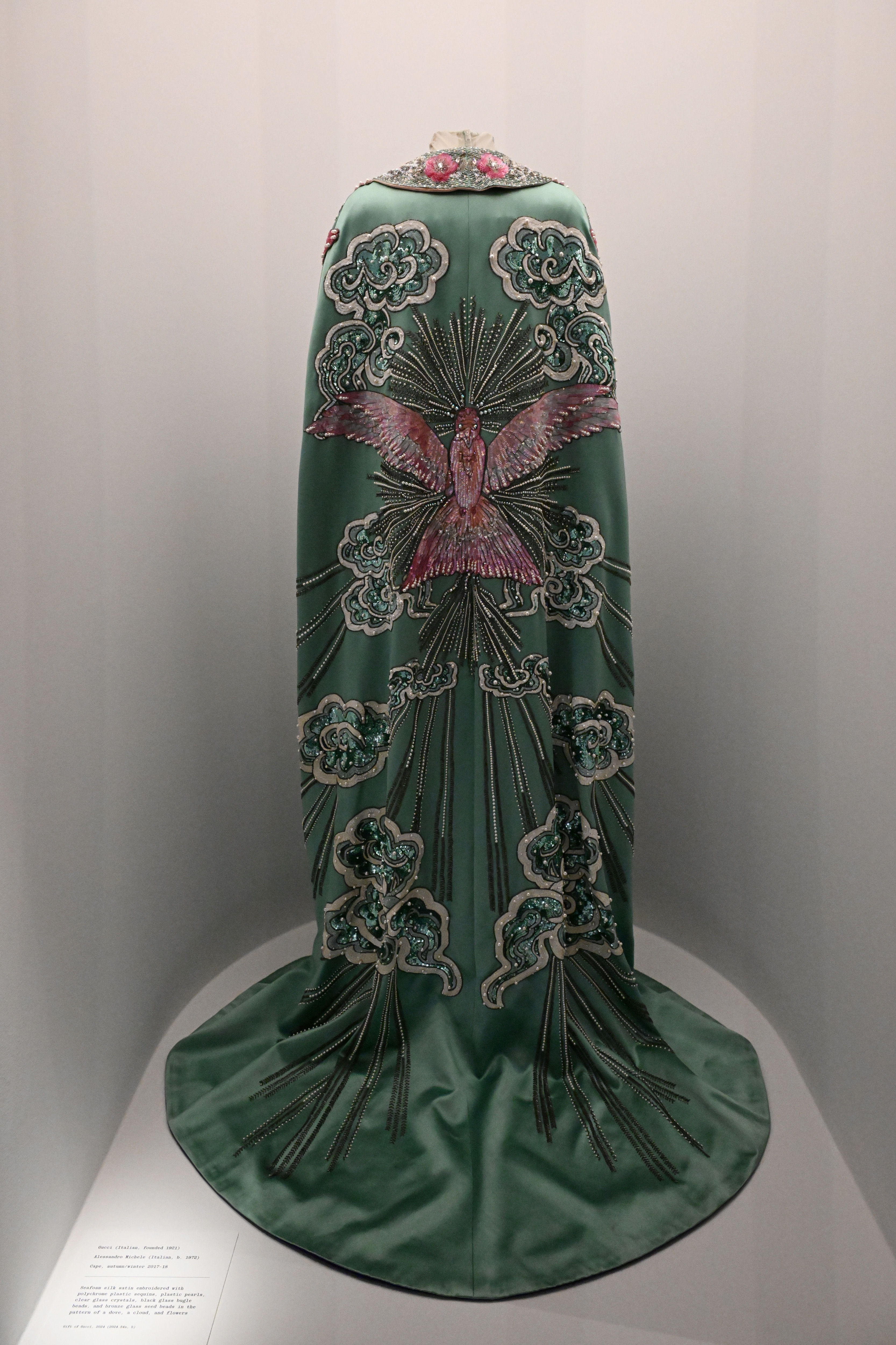 A displayed long-sleeve emerald dress with intricate bird embroidery and a trail