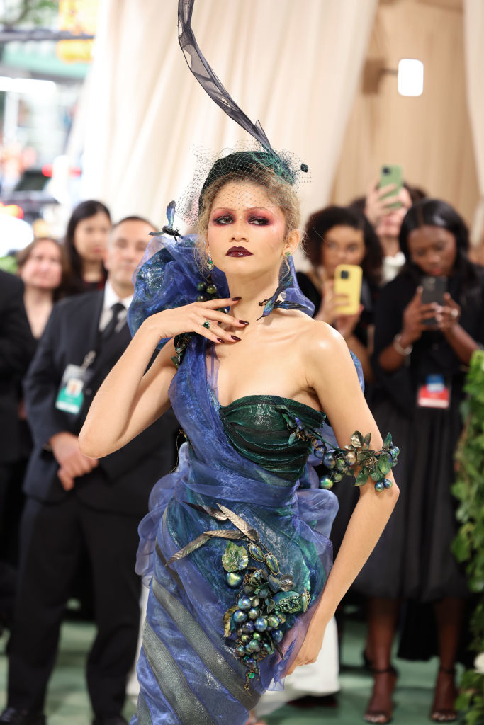 Zendaya in ornate blue-themed outfit with structured design elements and headpiece, posing at event
