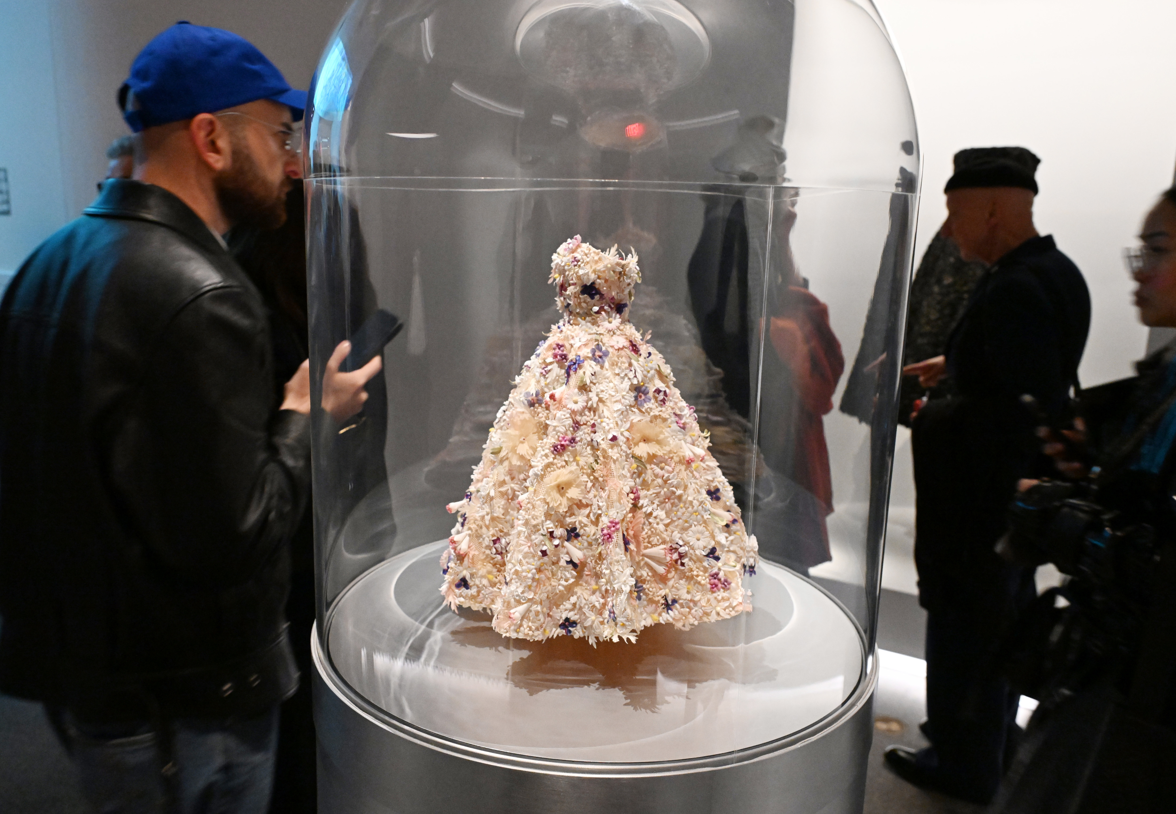 Man viewing a glass-enclosed ornate gown on display. No persons in the image are identifiable