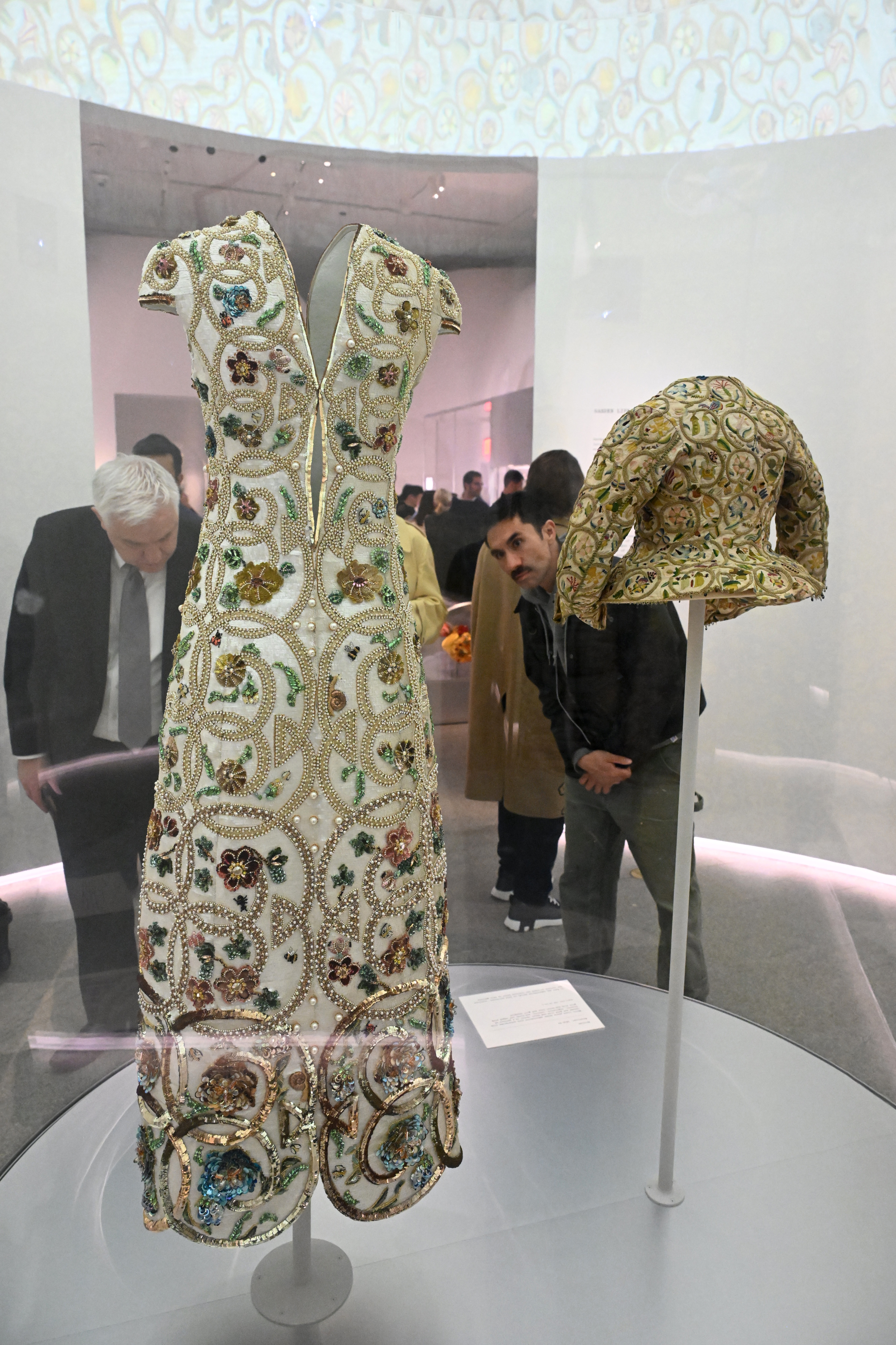 Vintage dress and jacket on display, intricate beadwork, visitors observing exhibit in background