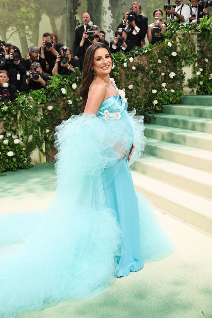 Pregnant Lea Michele poses in a flowing blue gown with tulle overlay, photographers in the background