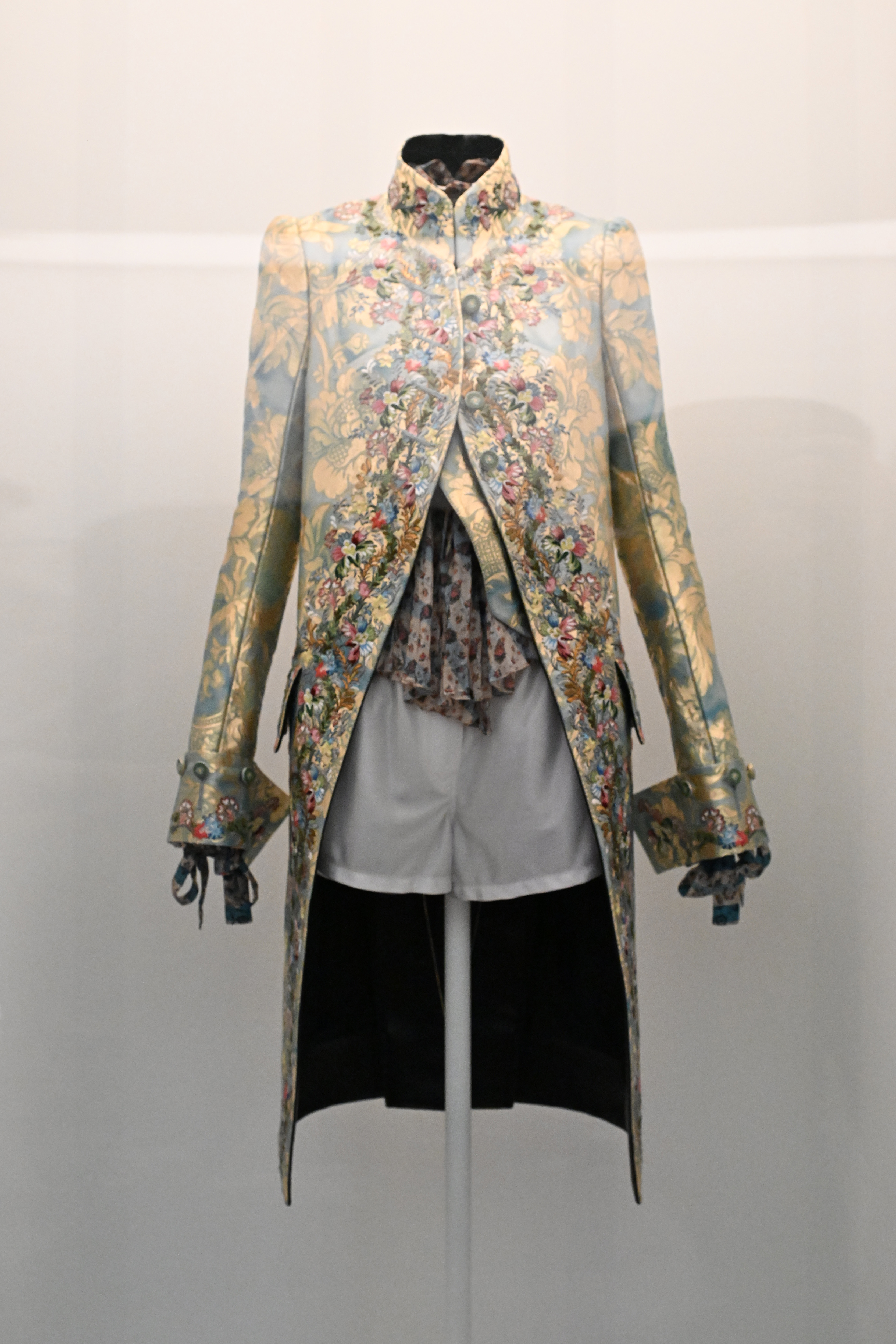 Elaborate floral embroidered coat displayed on a mannequin with a black skirt and white blouse