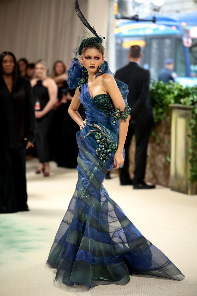 Zendaya in an elaborate blue tiered gown and headpiece posing on an event runway