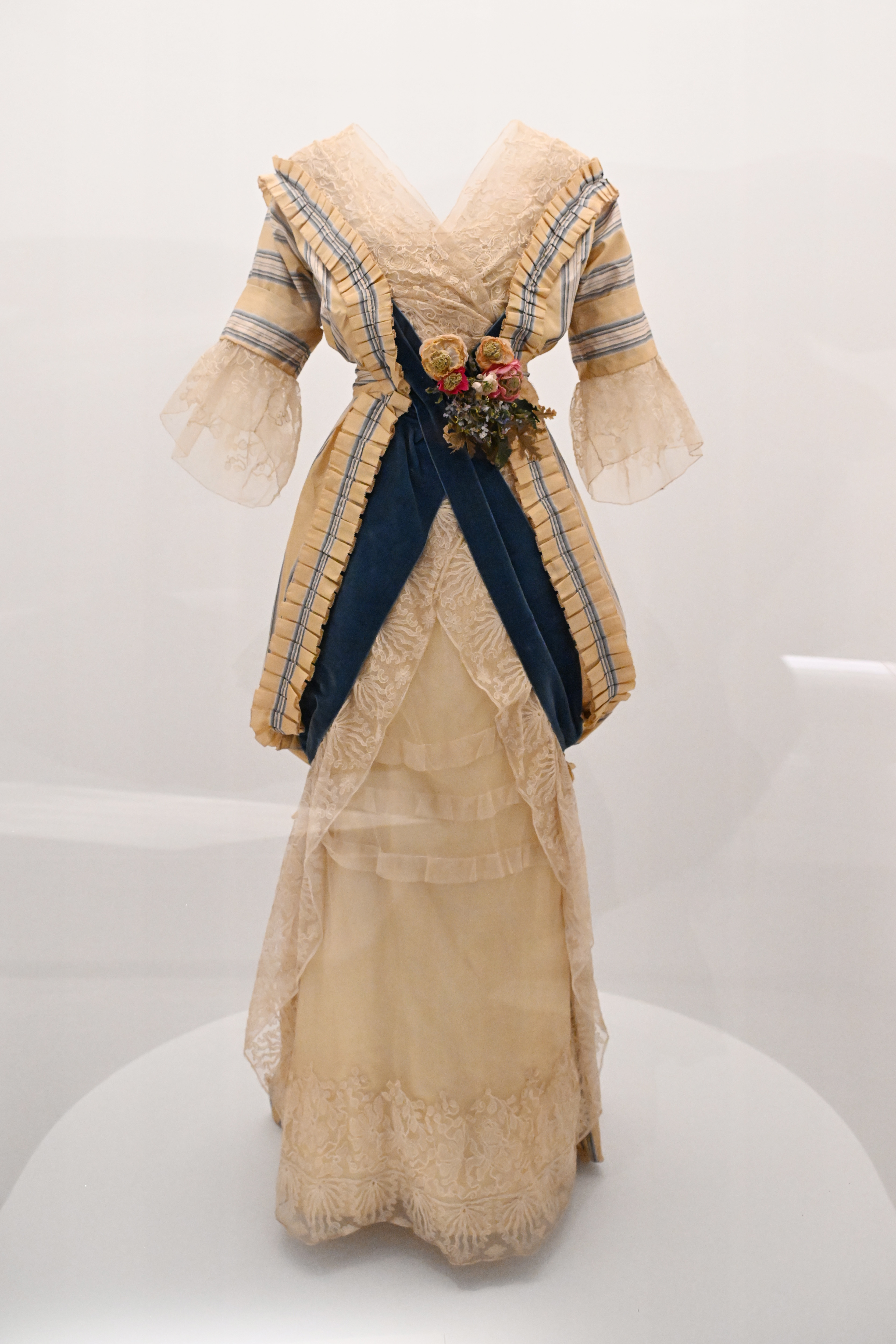Vintage dress on display with lace details, striped accents, and a floral adornment