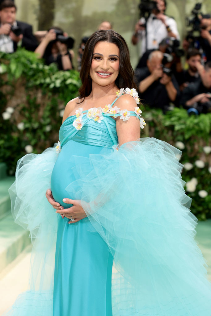 A pregnant Lea Michele in a tulle gown with floral accents, smiling on the Met Gala steps