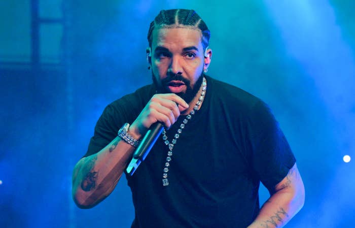 Drake performing on stage, wearing a black t-shirt and chains, holding a microphone