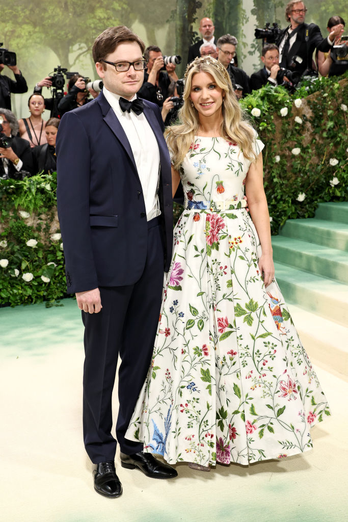 Charles in a tuxedo and Elizabeth in a floral gown posing together at an event with photographers in the background
