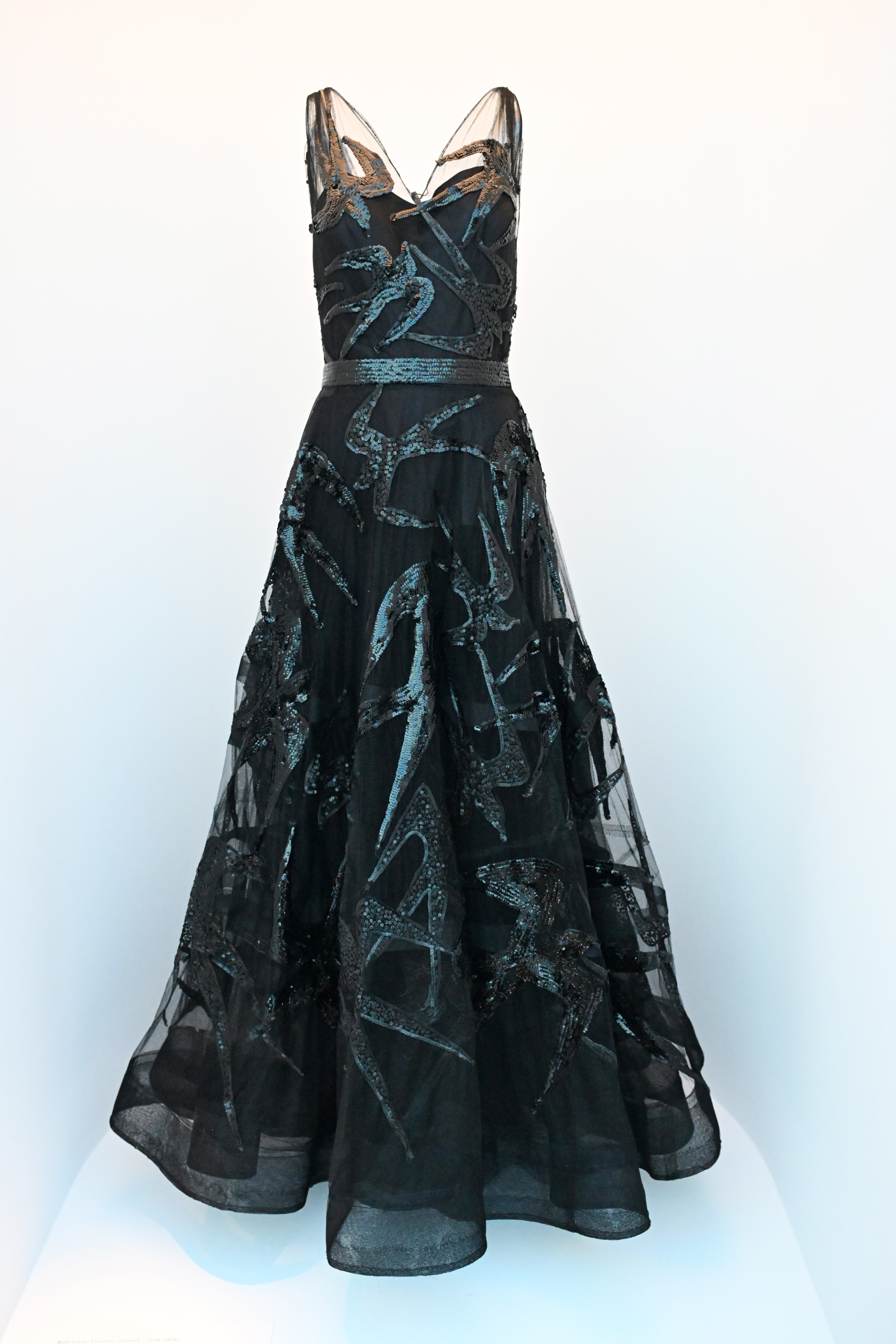 Elegant black evening gown with intricate lace detail on a mannequin. No persons present