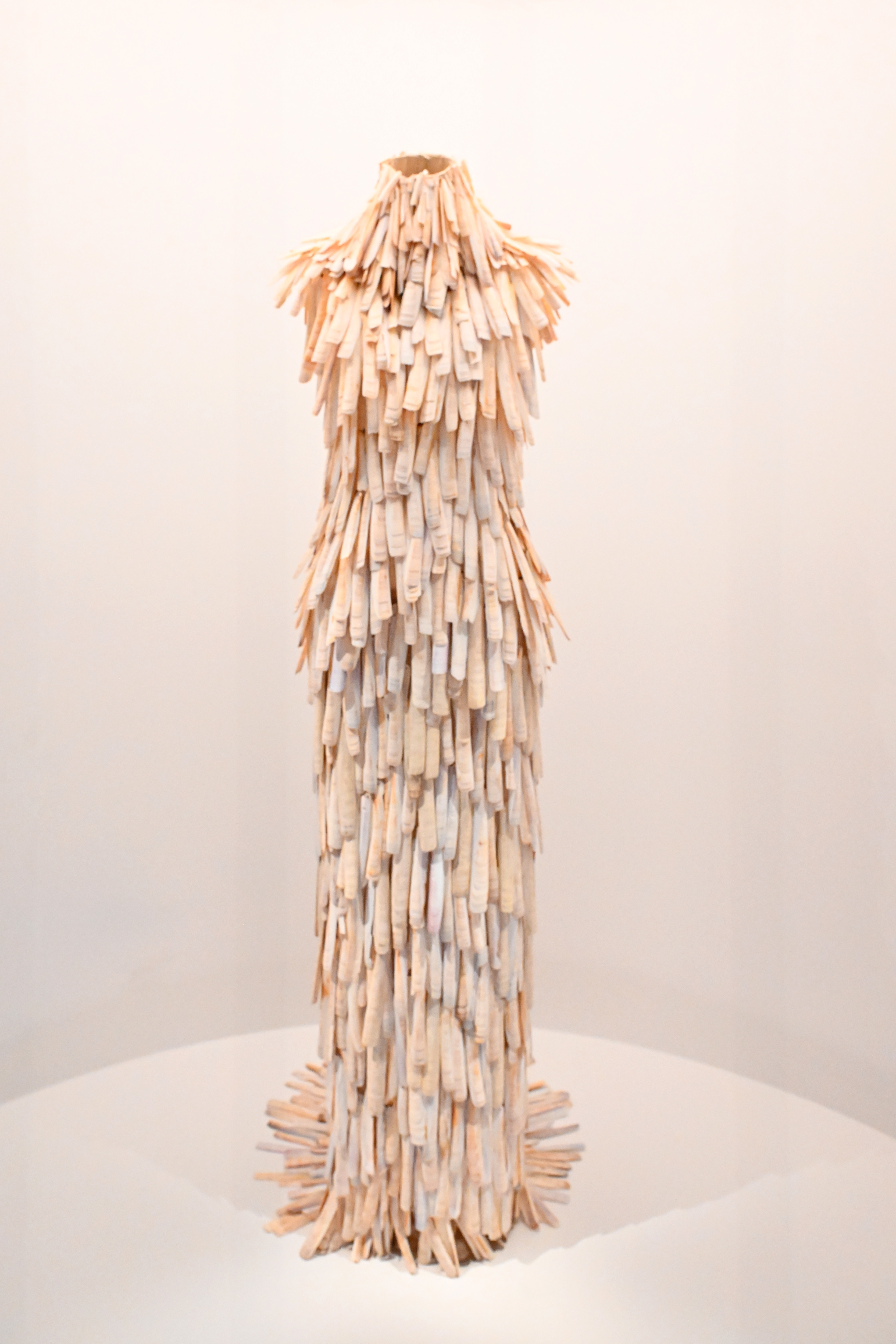 Sculptural dress made of layered material on a mannequin, displayed in a gallery setting