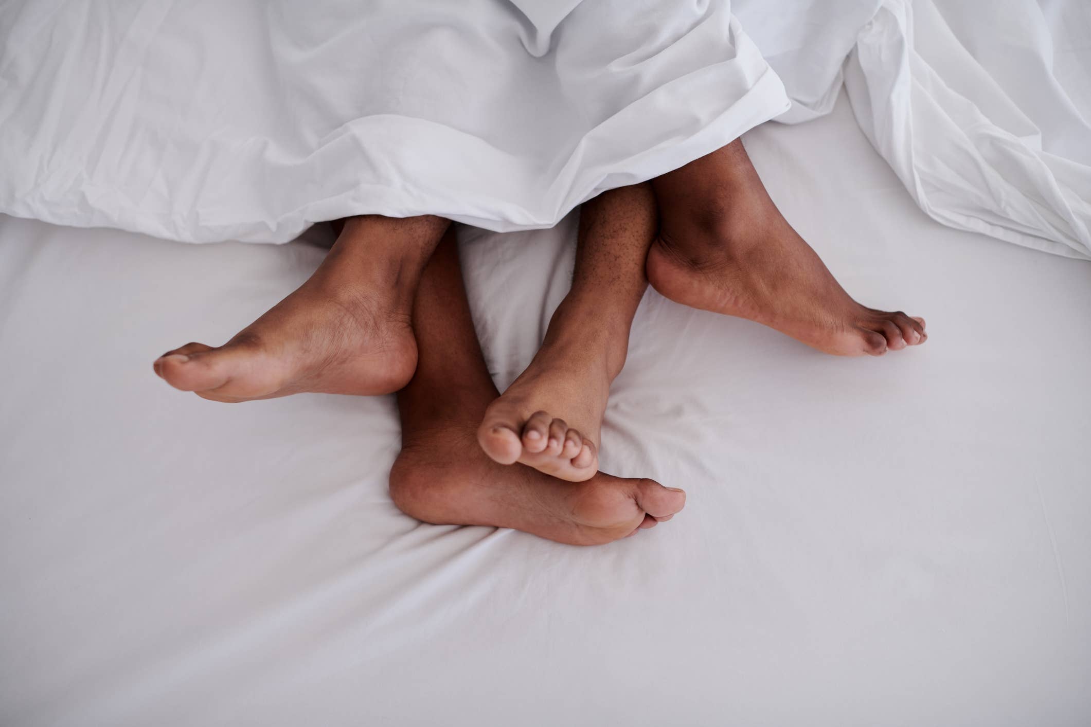 Two pairs of feet intertwined under white bedding, implying intimacy