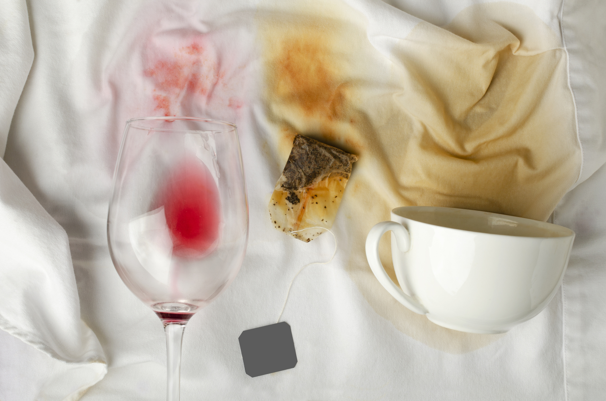A spilled glass of wine next to a tea bag on a bed, portraying a minor domestic accident