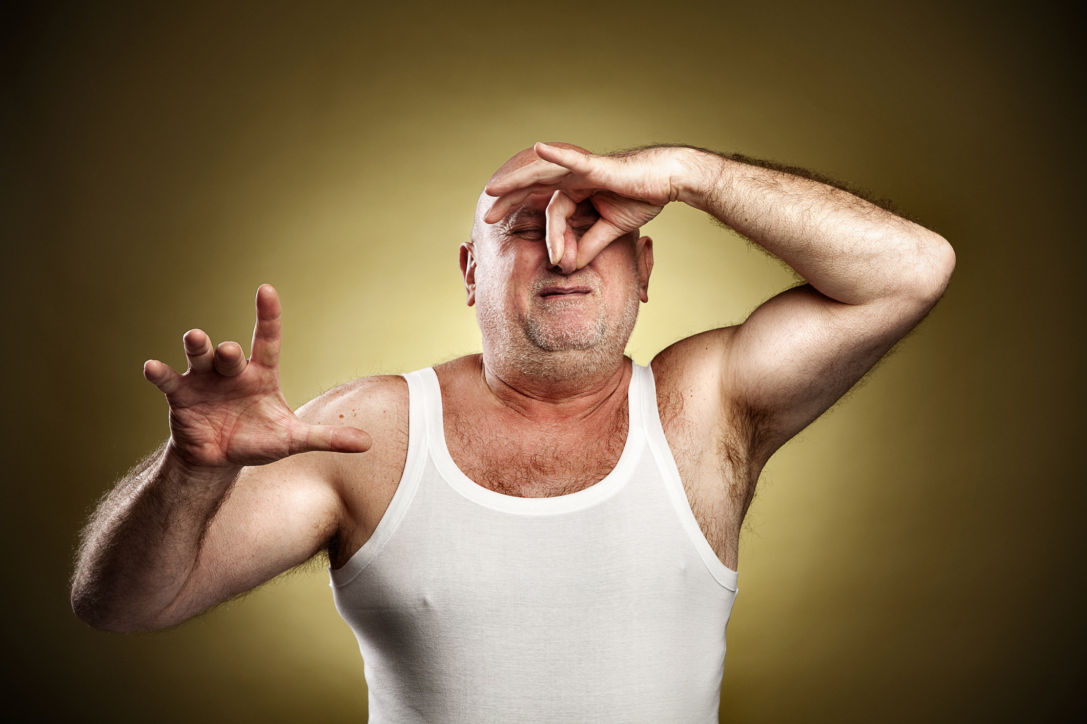 Man in white tank top making a pinching gesture near his eyes with a pained expression