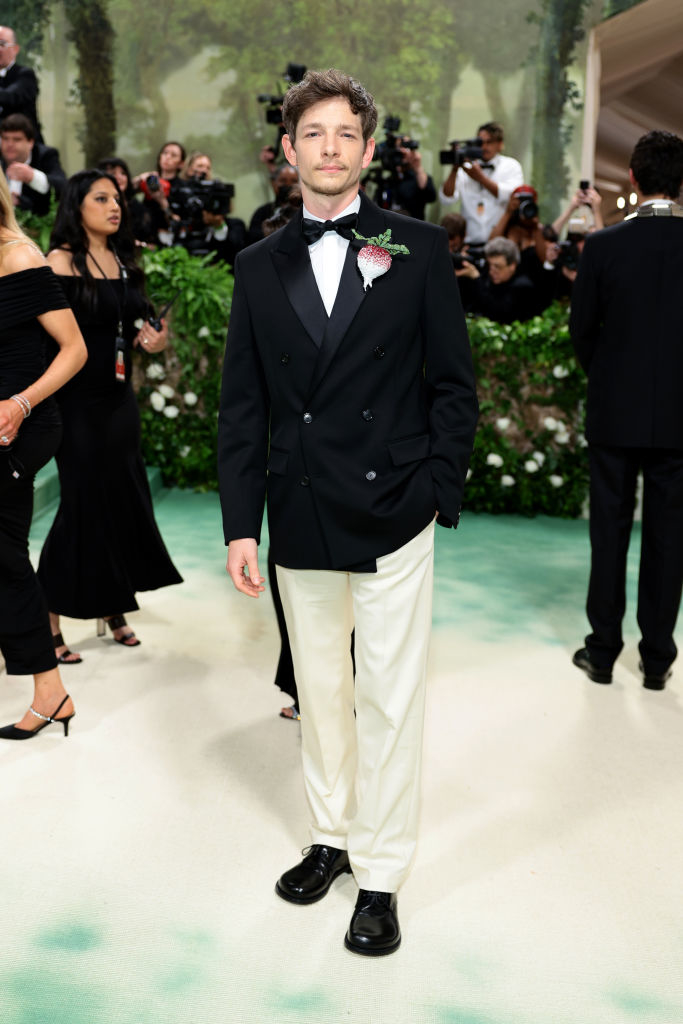 Mike Faist in a black tuxedo jacket with white pants and bow tie posing on a gala event carpet