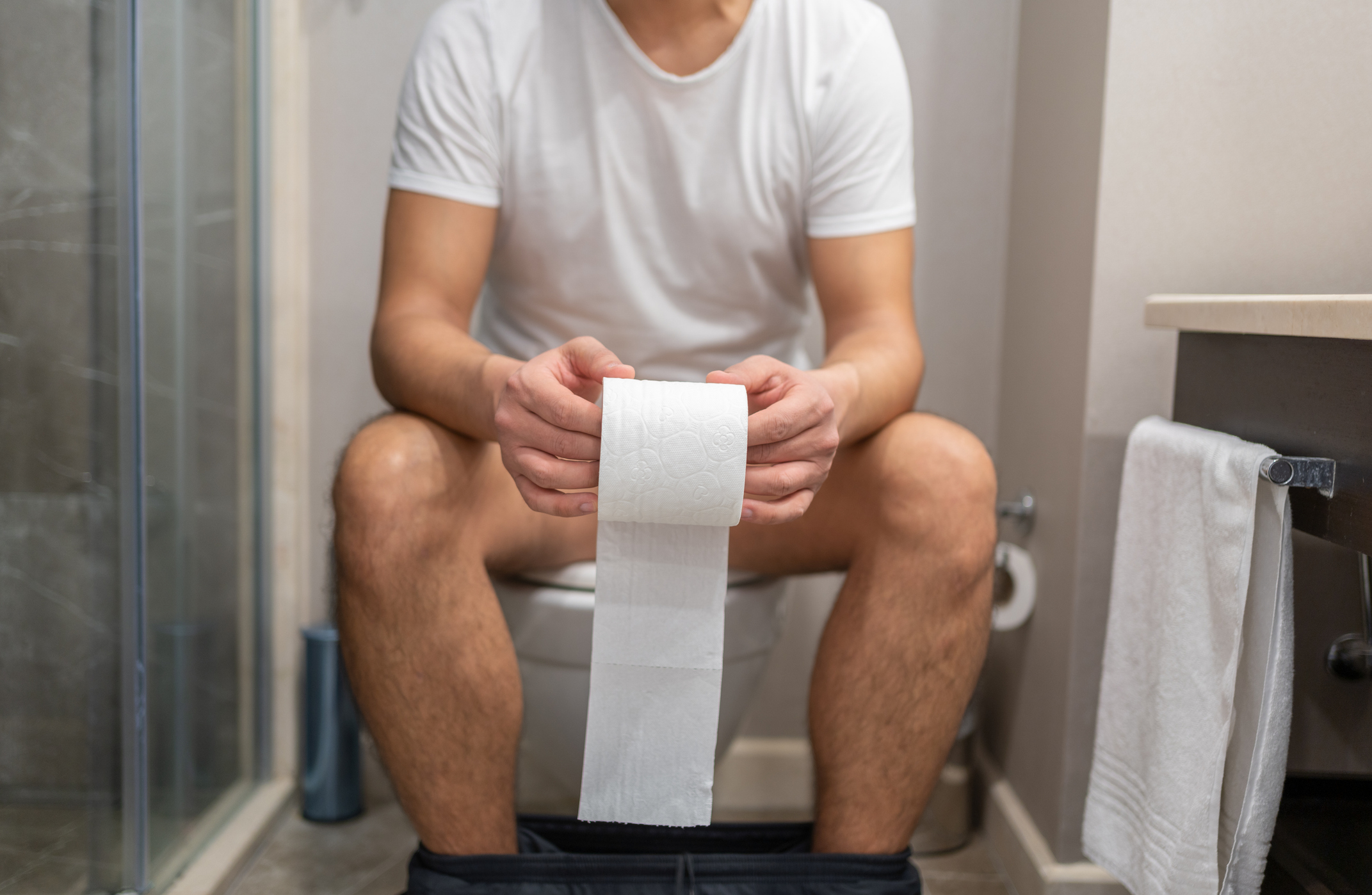 Person sitting on a toilet holding a roll of toilet paper, appearing perplexed