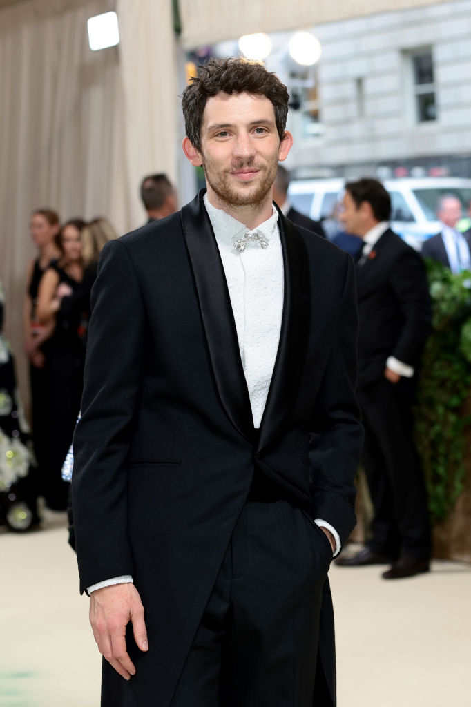 Josh O'Connor in a black suit with bow tie, smiling on a red carpet