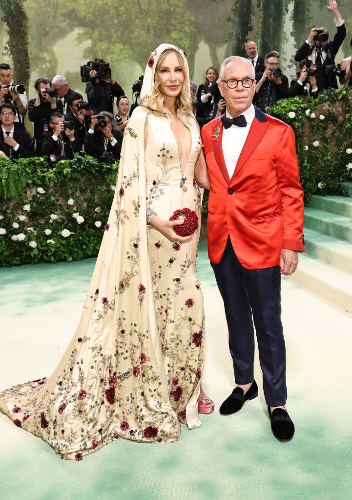 Dee in a floral patterned gown with a train, Tommy in a jacket and bow tie, photographers behind them