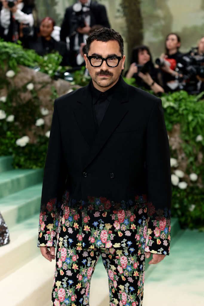 Dan Levy in double-breasted jacket and floral trousers stands at event