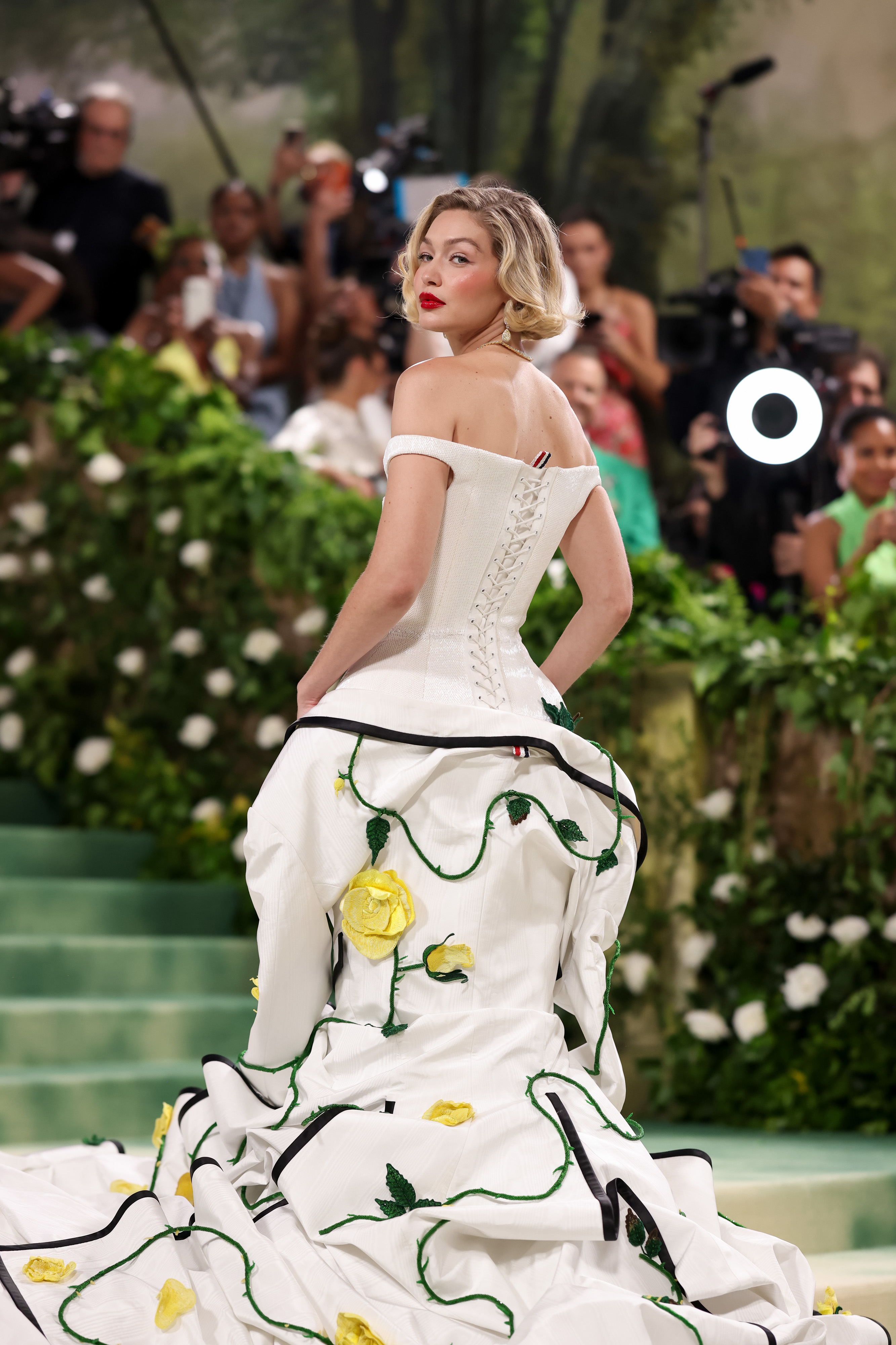 Celebridad en vestido blanco estilo corsé con detalles de rosas, posando en alfombra de evento