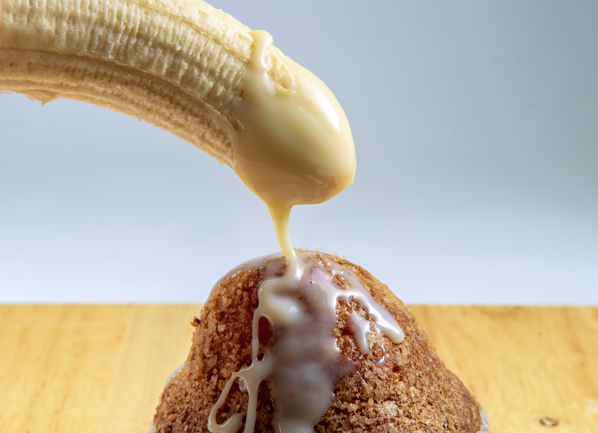 Condensed milk being poured onto a cinnamon muffin from a peeled banana