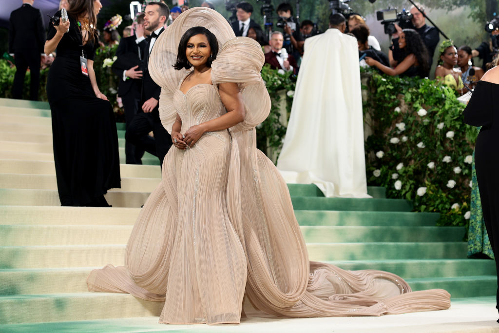 Mindy Kaling poses in a layered gown with a flowing train at an event