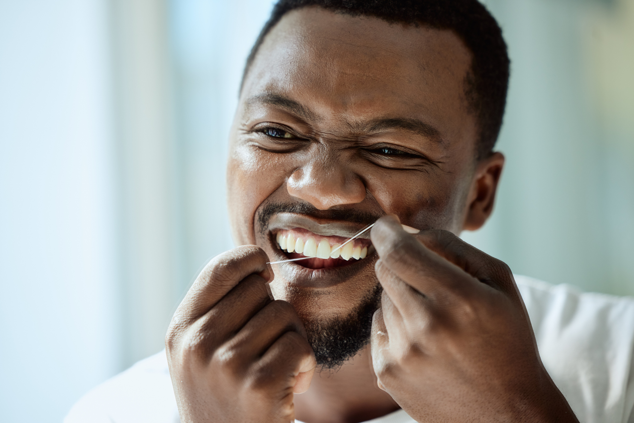 Man flossing his teeth, close-up, smiling, with focus on dental hygiene