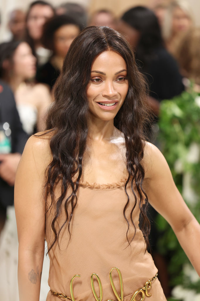 Zoe Saldana in a beige dress with unique waist detailing posing at an event