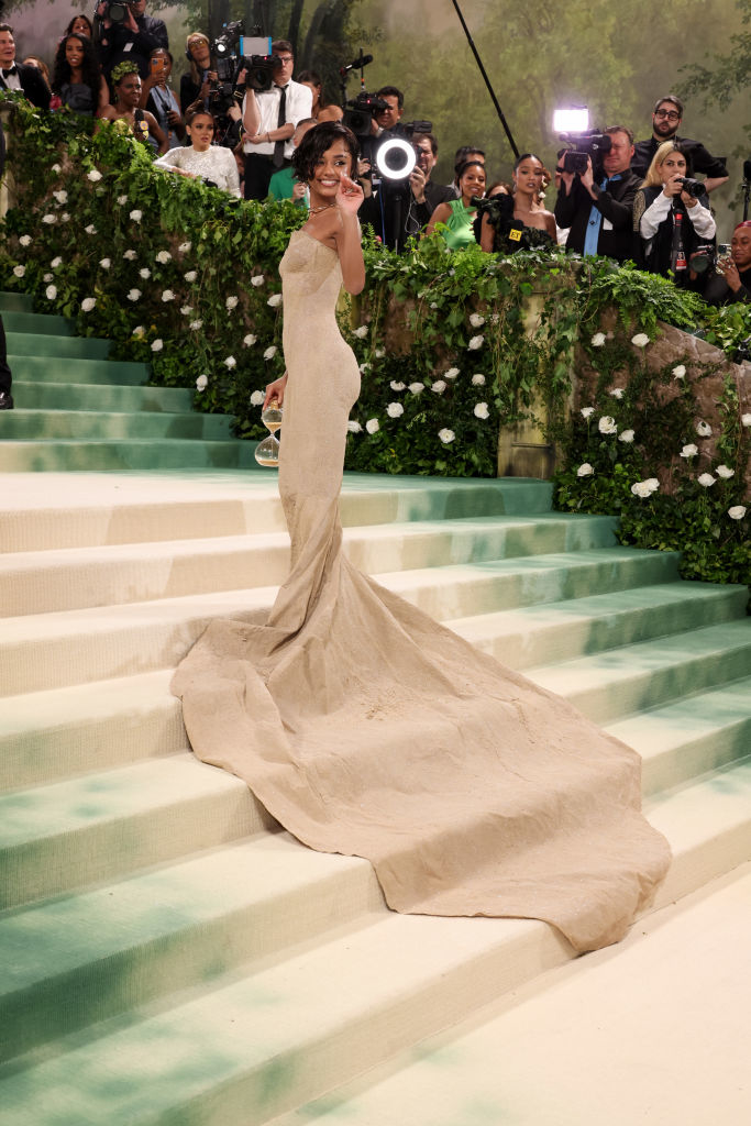 Tyla in elegant gown with long train posing on steps at a gala, photographers in background