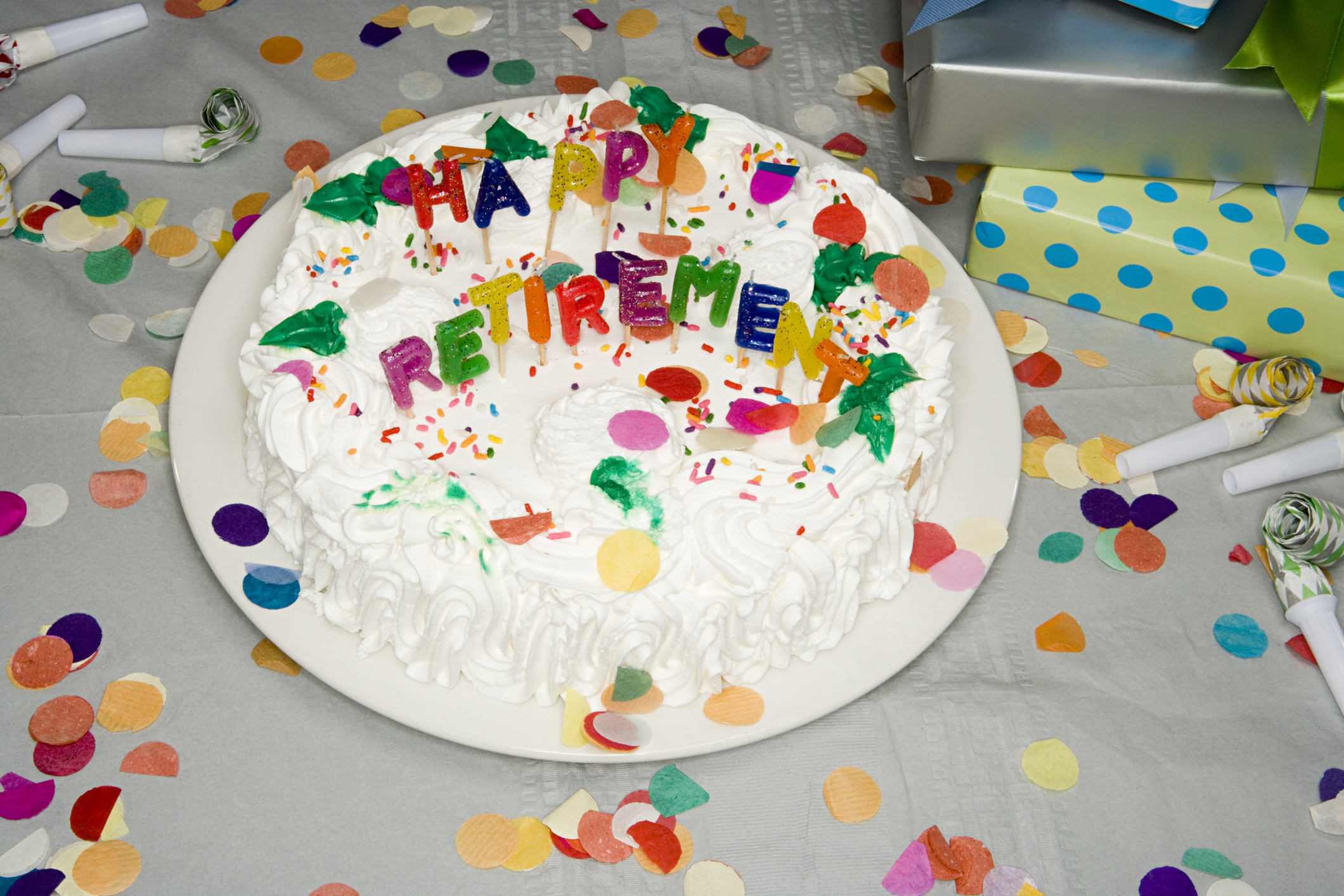 A retirement cake with &quot;Happy Retirement&quot; lettering surrounded by confetti and party blowers on a table