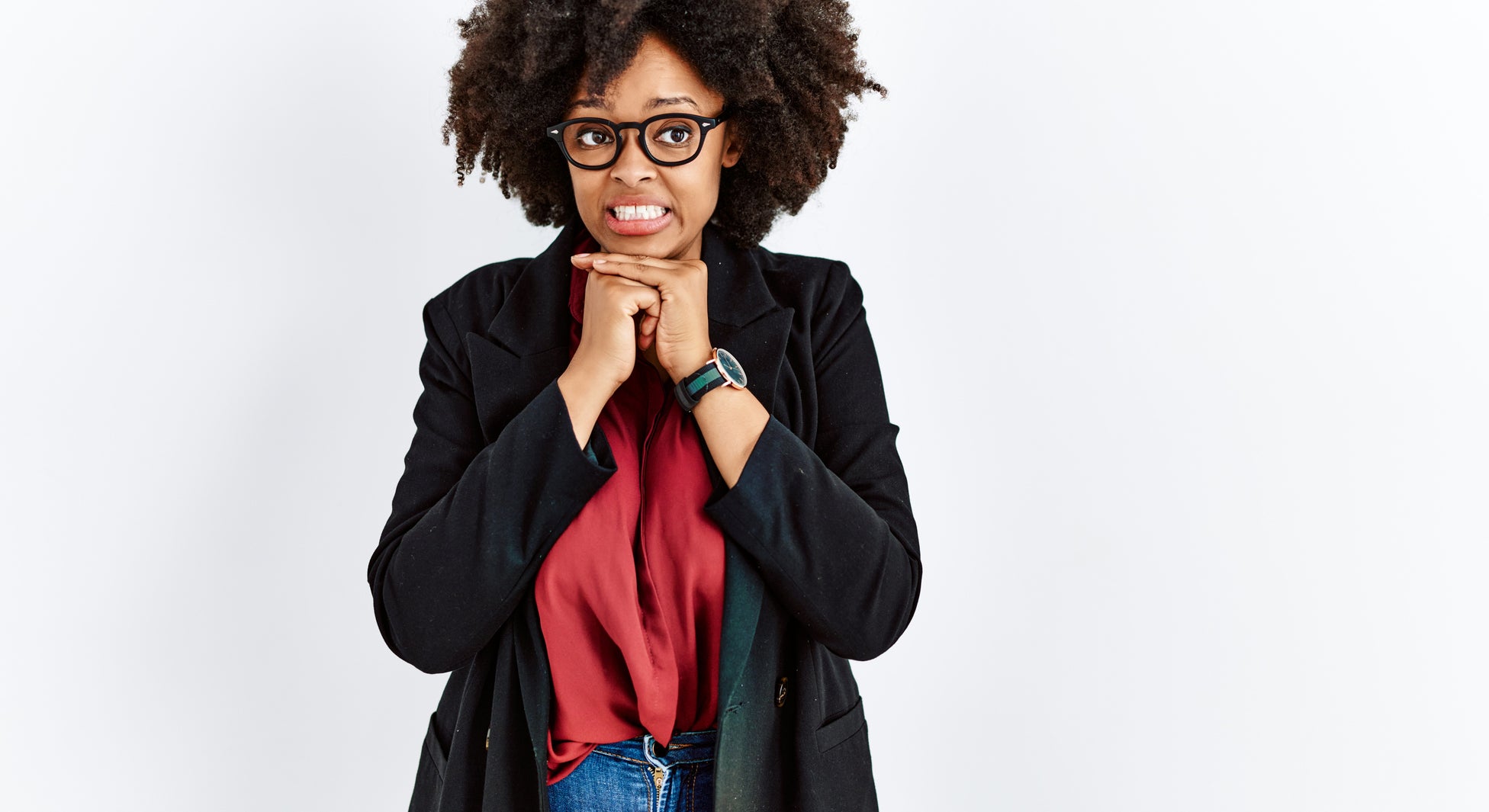 Woman with curly hair, glasses, biting fingernails in anxious pose, wearing a blazer, red top, and jeans