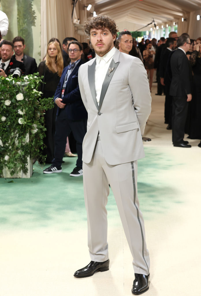 Jack Harlow in a tailored gray suit with stripe detail, hands in pockets at an event