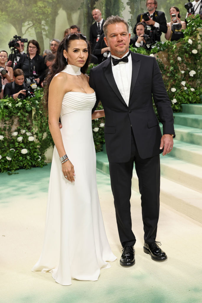 Luciana Barroso and Matt Damon pose together; the woman wears an elegant white gown, the man in a classic tuxedo