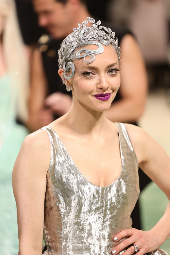 Amanda Seyfried person wearing a metallic gown and intricate headpiece with a confident smile